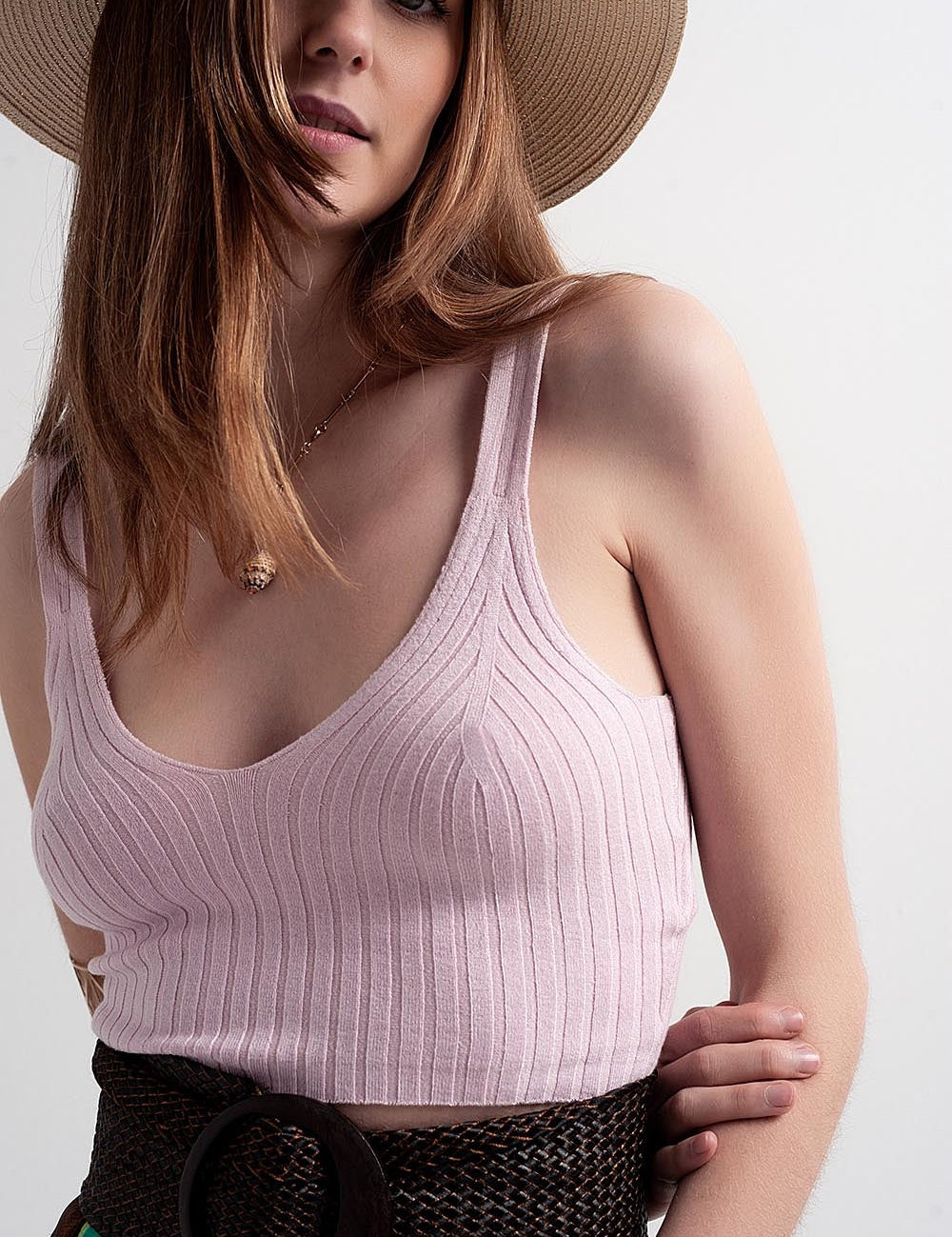 Woman wearing Evarie knit co-ord top in sun-washed pink with a v-neck, paired stylishly with a hat and belt for a chic look.