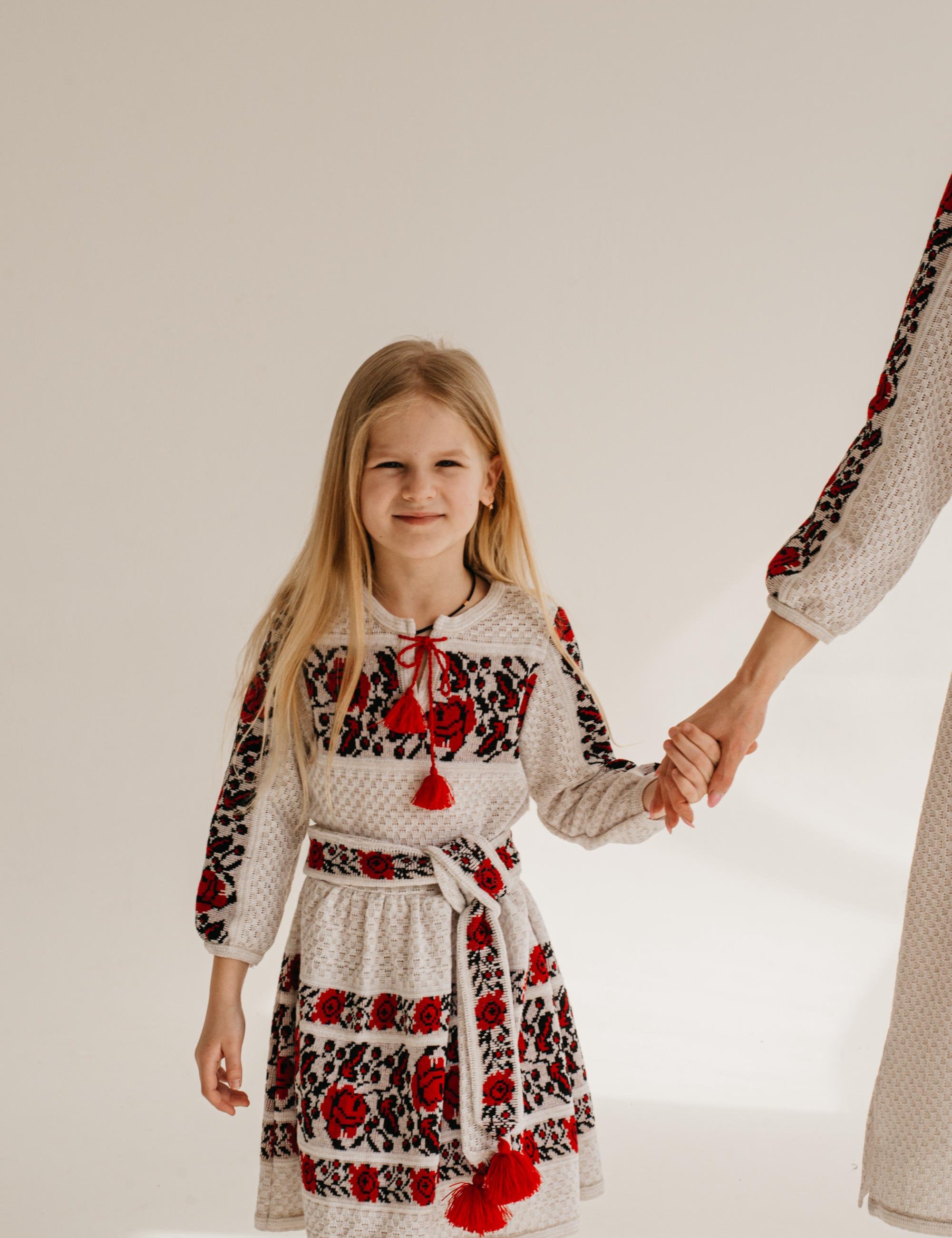 Girl in embroidered Ukrainian dress holding hand, showcasing cultural attire and traditional knit design.