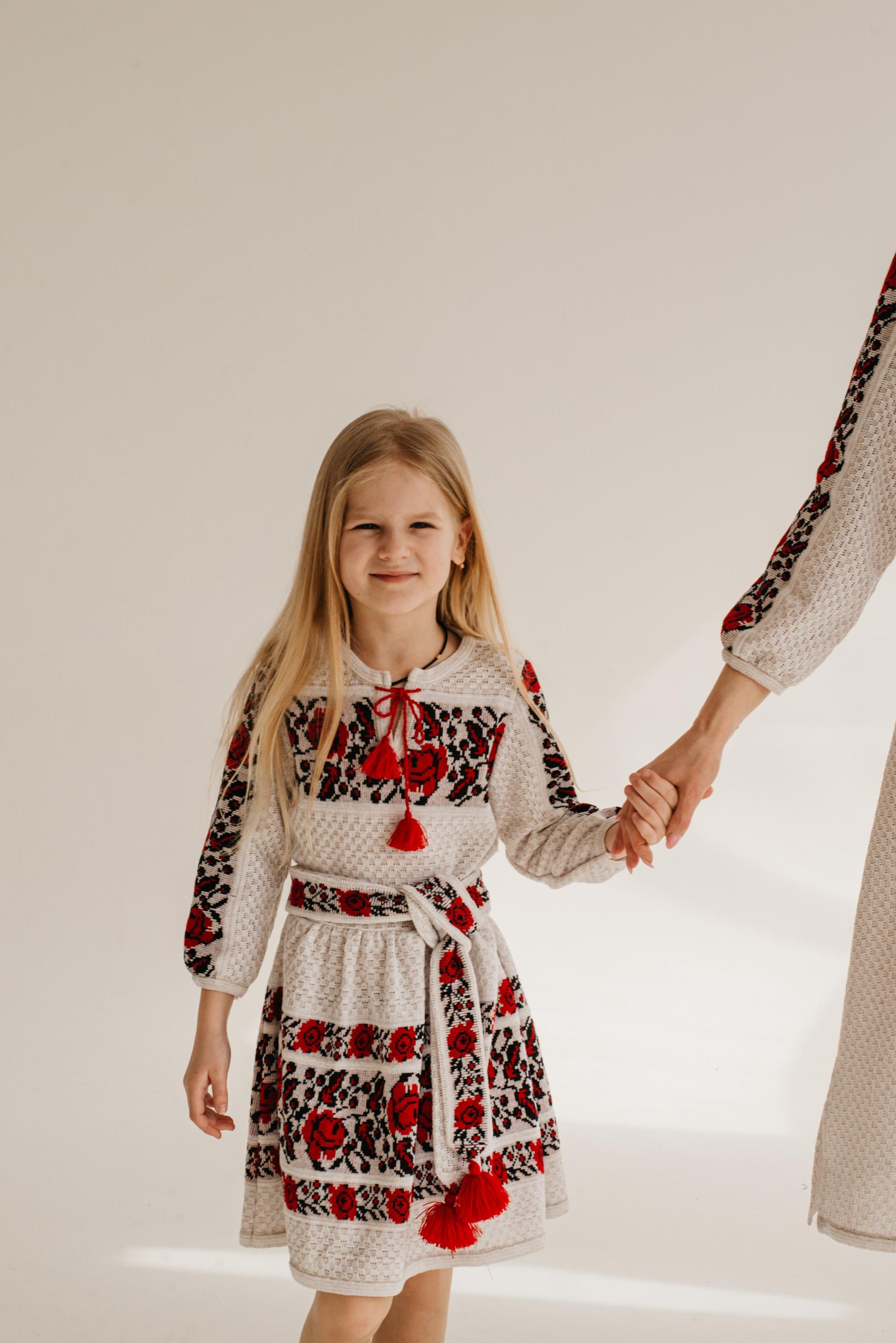 Girl in embroidered Ukrainian dress holding hand, showcasing cultural attire and traditional knit design.