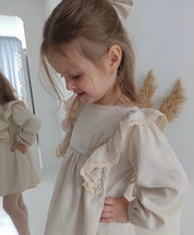 Little girl wearing a light beige linen dress with ruffled sleeves, reflecting simplicity and charm.