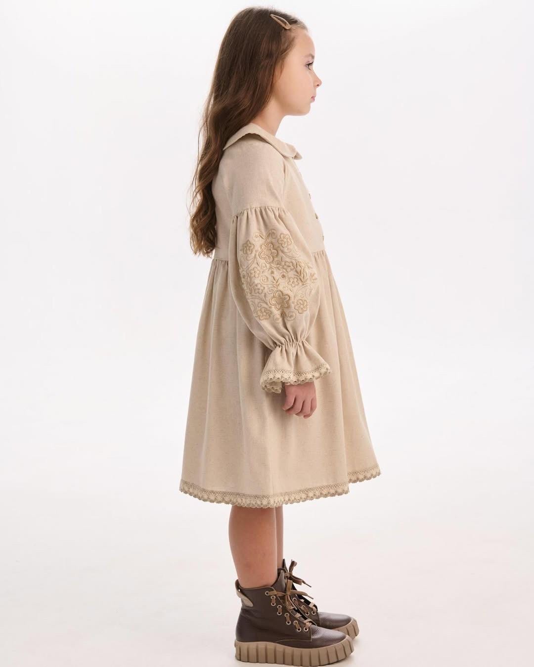 Side view of a girl wearing a beige embroidered linen dress, showcasing Ukrainian folk motifs, highlighting Ukrainian craftsmanship