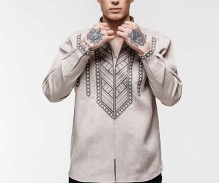 Person wearing a traditional embroidered shirt with intricate tattoo designs on their hands, showcasing cultural fashion and artistry.