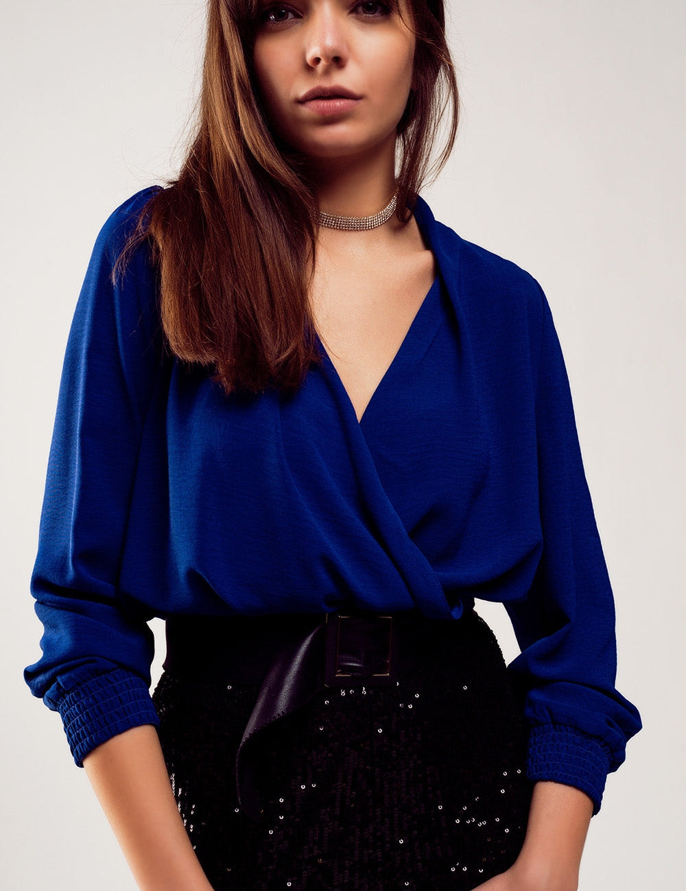 Woman wearing Alcenyra Wrap Satin Blouse in luminous blue with V-cut collar and shirred cuffs, paired with black sequin skirt.