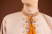 Close-up of men's embroidered Vyshyvanka shirt with intricate Ukrainian design, featuring orange and white patterns on a beige fabric.