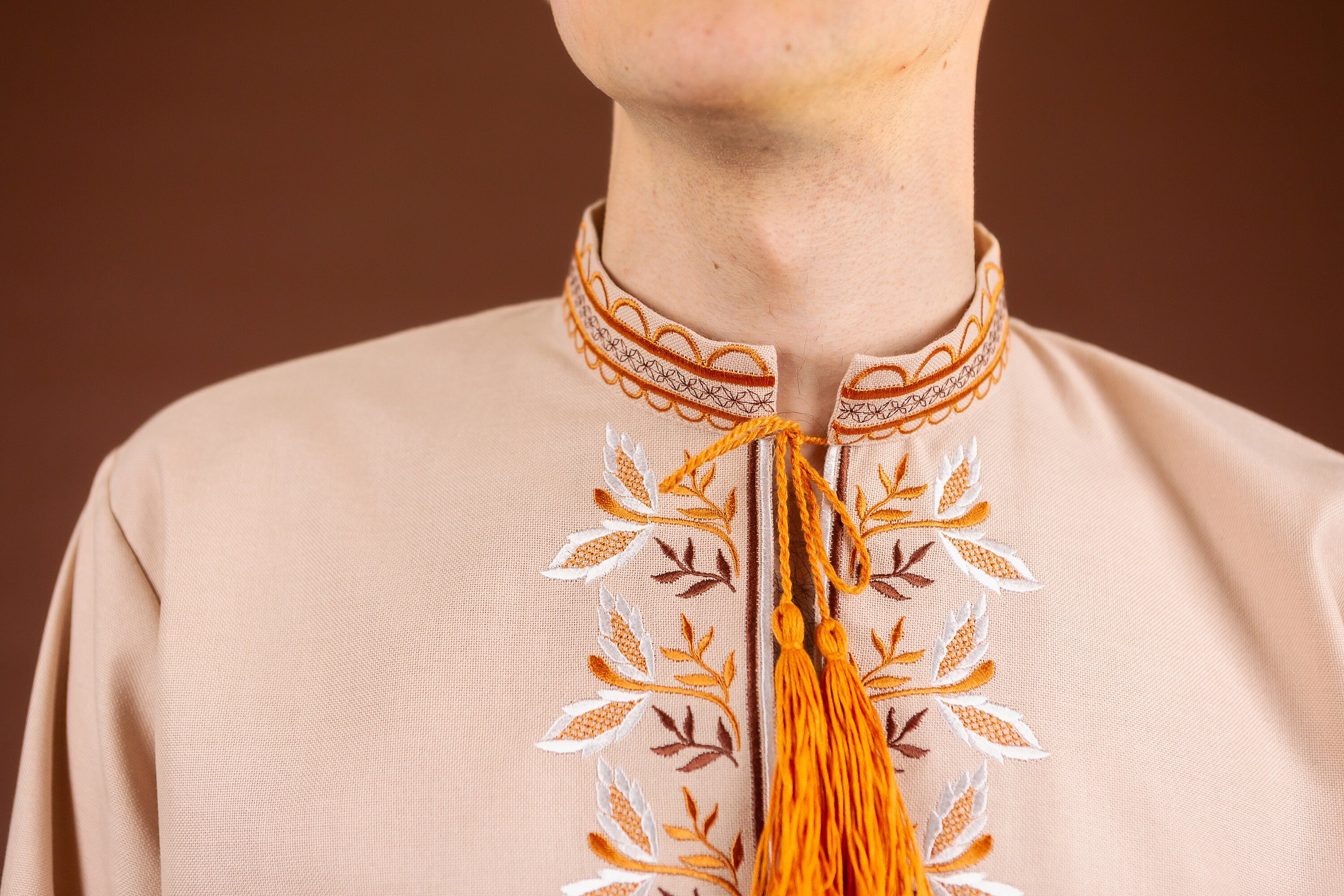 Close-up of men's embroidered Vyshyvanka shirt with intricate Ukrainian design, featuring orange and white patterns on a beige fabric.