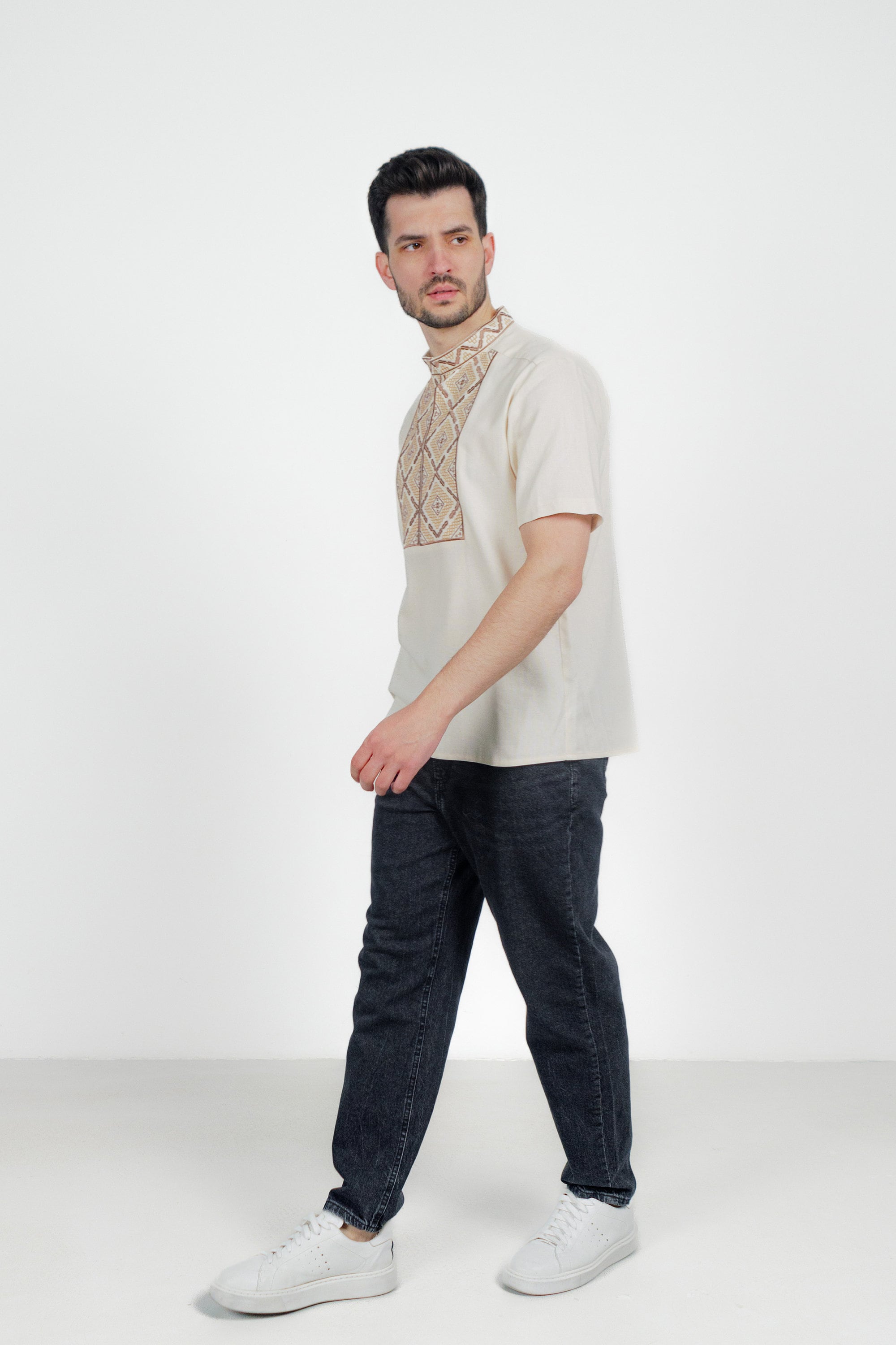 Man wearing a traditional Ukrainian embroidered linen shirt with geometric pattern and short sleeves, styled with jeans.