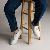 Person wearing Gold Ukrainian Trizub Slip-On Canvas Shoes sitting on a wooden stool, showcasing style and comfort.