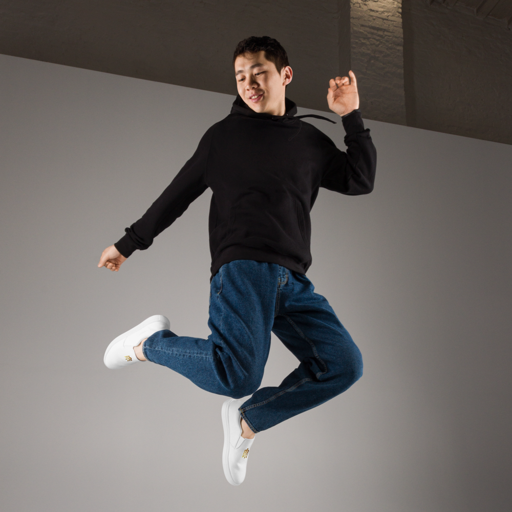 Person jumping in style wearing Gold Ukrainian Trizub slip-on canvas shoes with a black top and blue jeans.