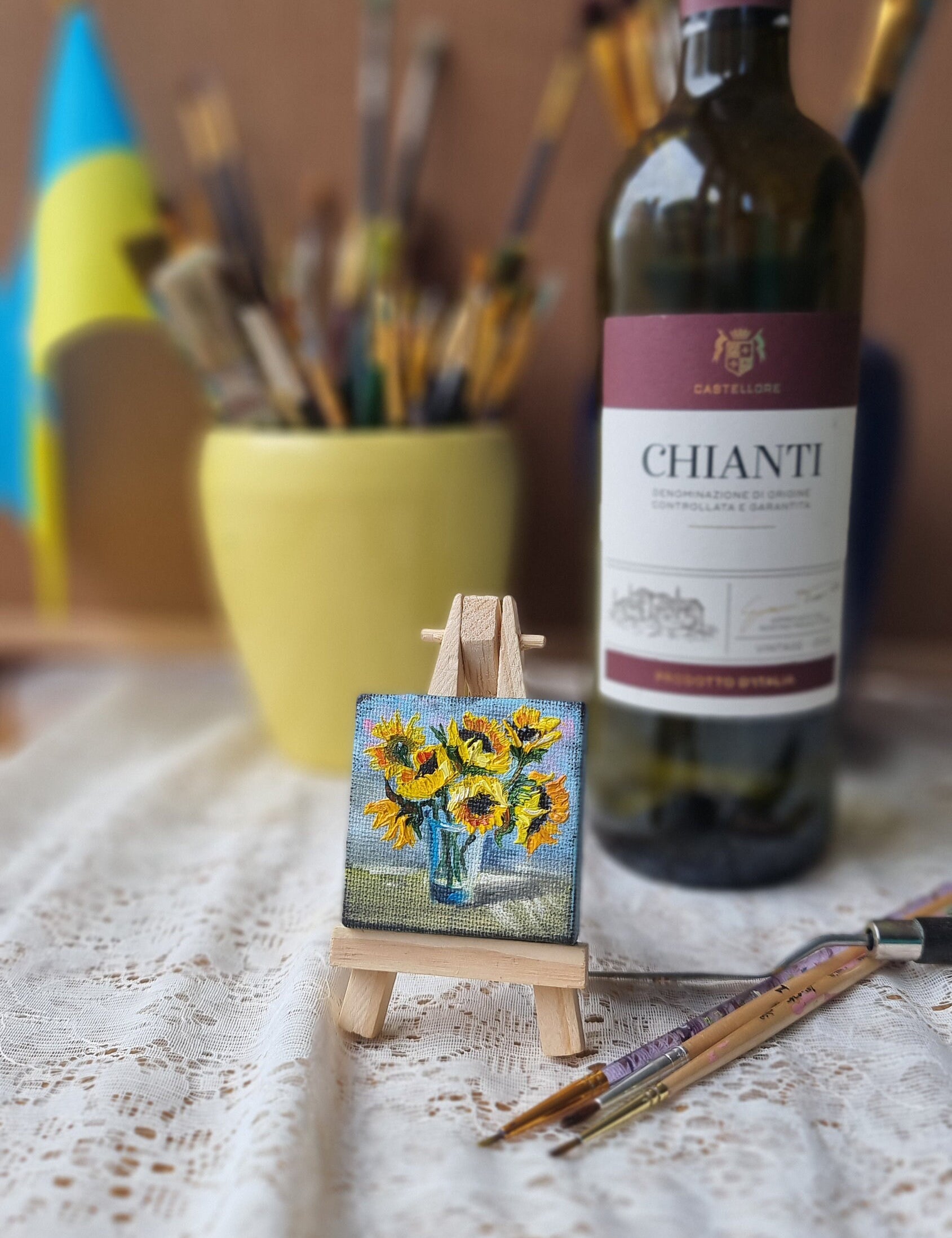 Miniature sunflower oil painting on easel, Ukrainian art, with wine bottle and brushes in the background.
