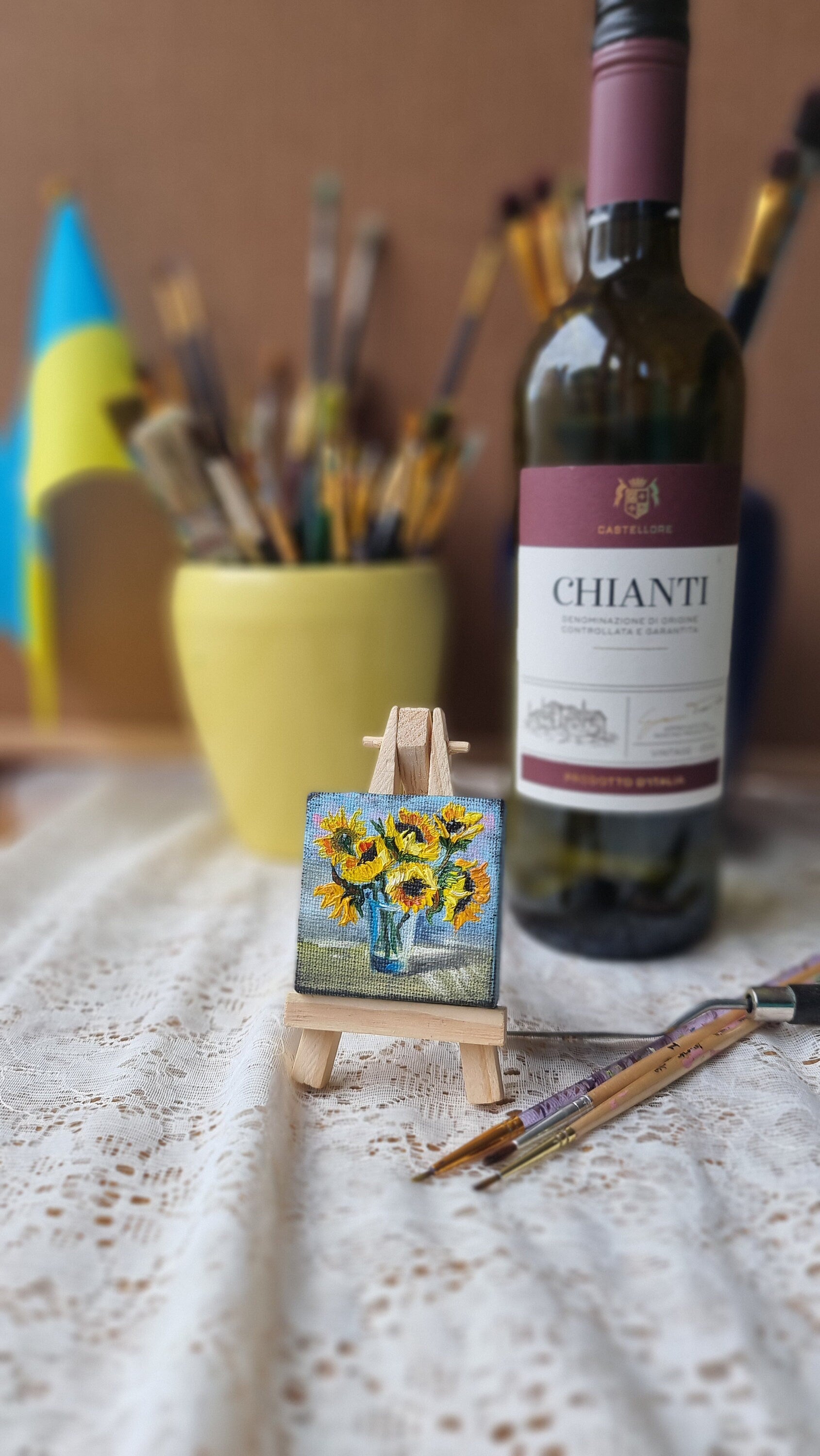 Miniature sunflower oil painting on easel, Ukrainian art, with wine bottle and brushes in the background.