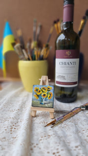 Miniature sunflower oil painting on easel, Ukrainian art, with wine bottle and brushes in the background.