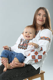 Mother and child wearing traditional Ukrainian vyshyvanka shirts with colorful embroidery, sitting indoors.