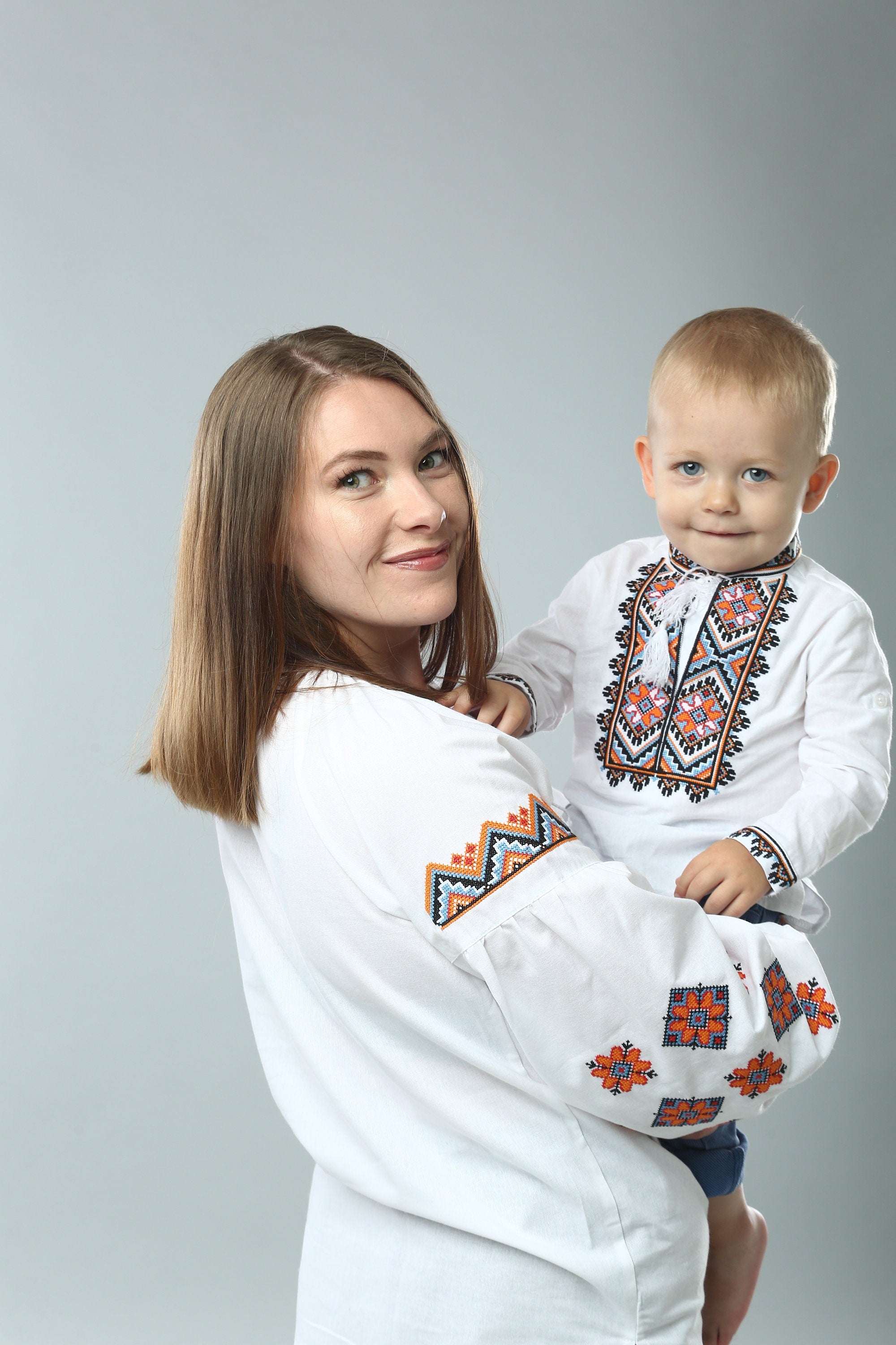 Mother holding child wearing traditional Ukrainian embroidered shirts, showcasing cultural clothing with vibrant patterns.