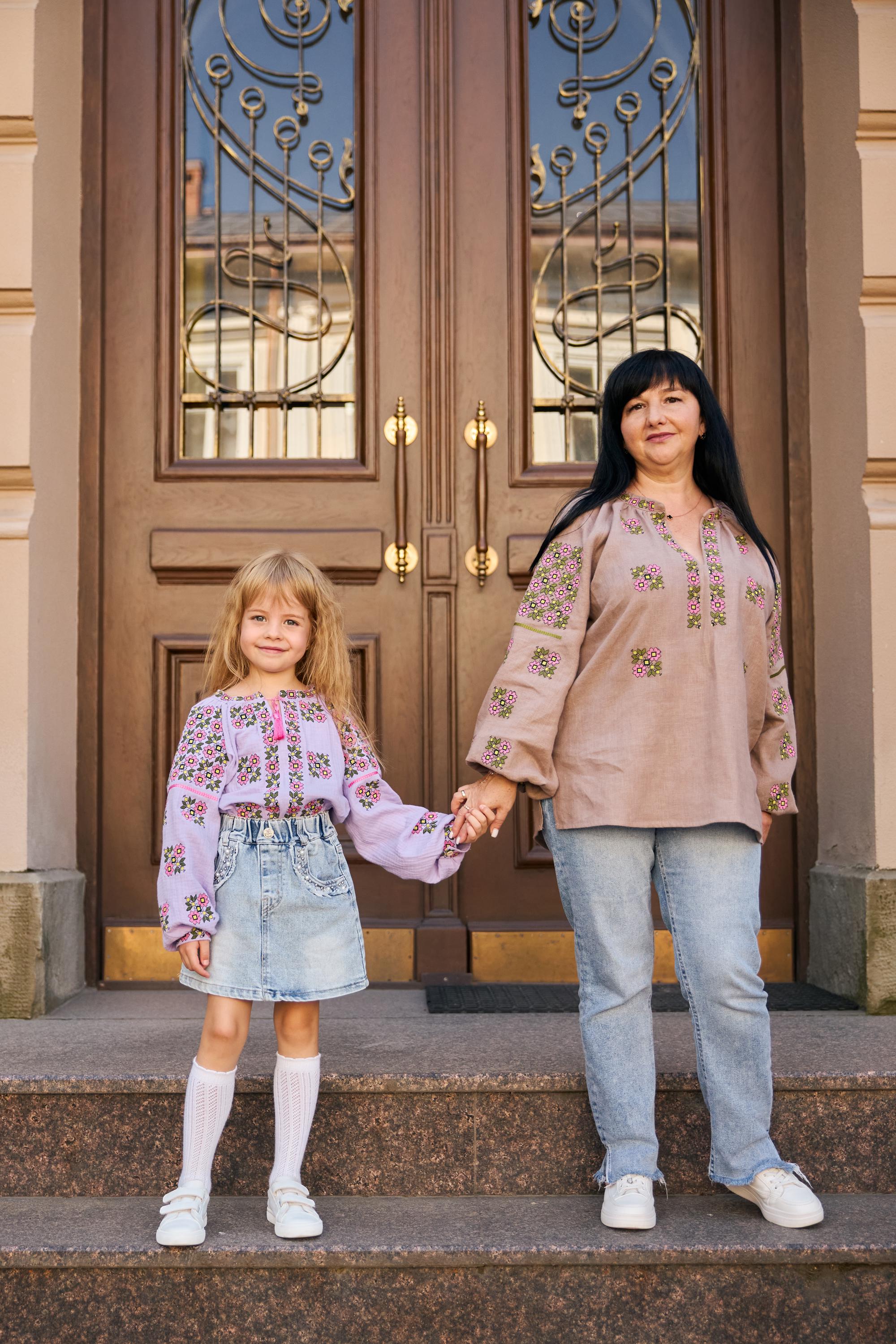 Mother and daughter wearing embroidered Ukrainian vyshyvanka blouses standing on steps in front of ornate wooden doors.
