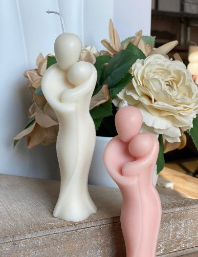 Sculptural candle depicting a nurturing embrace, made from organic soy wax, with floral decor backdrop.