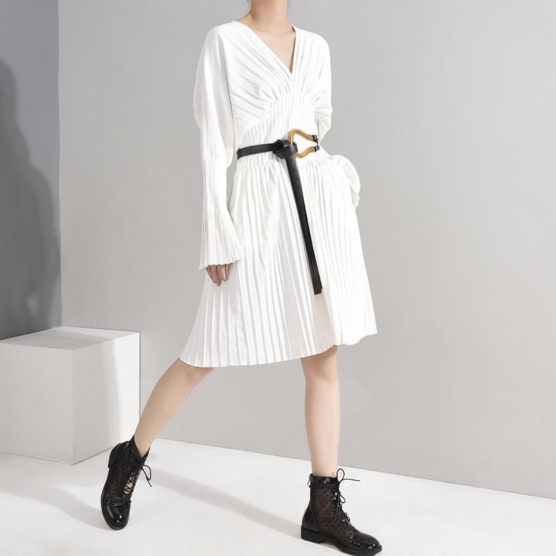 Naeris Pleated White Shirt Dress with V-neckline and long sleeves, styled with black ankle boots for a chic minimalist look.