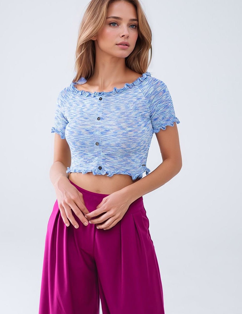 Model wearing a blue knit crop top with button detail, paired with vibrant magenta trousers, showcasing a stylish off-shoulder silhouette.