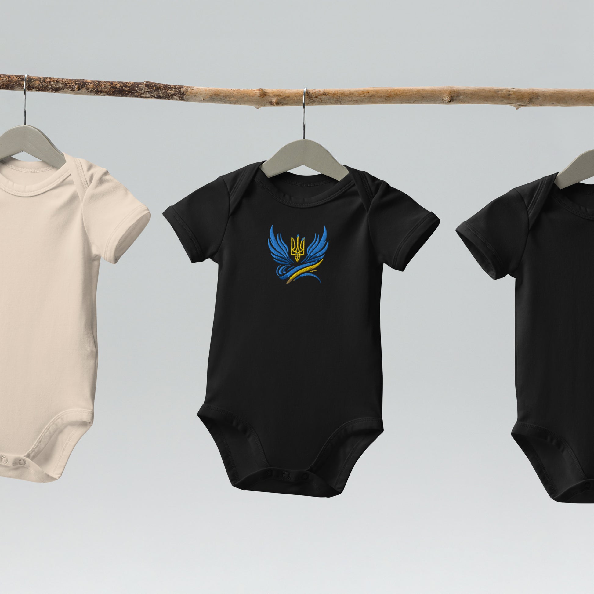 Black organic cotton baby bodysuit with Ukrainian Tryzub logo displayed on hanging rod.