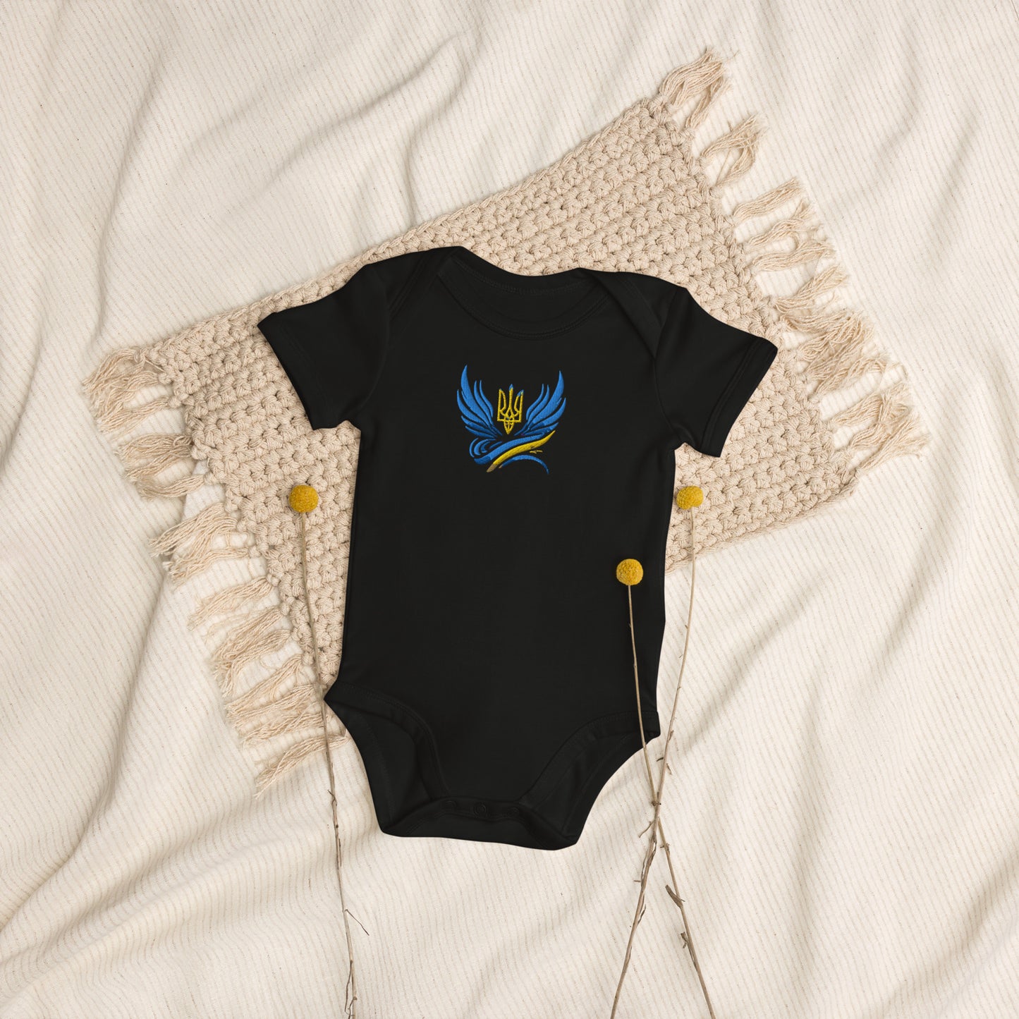 Organic cotton baby bodysuit with Ukrainian Tryzub logo on a blanket, showcasing comfort and style.