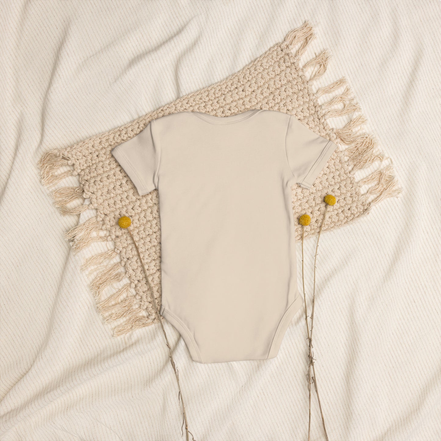 Organic cotton baby bodysuit with Ukrainian Tryzub logo on textured blanket background.