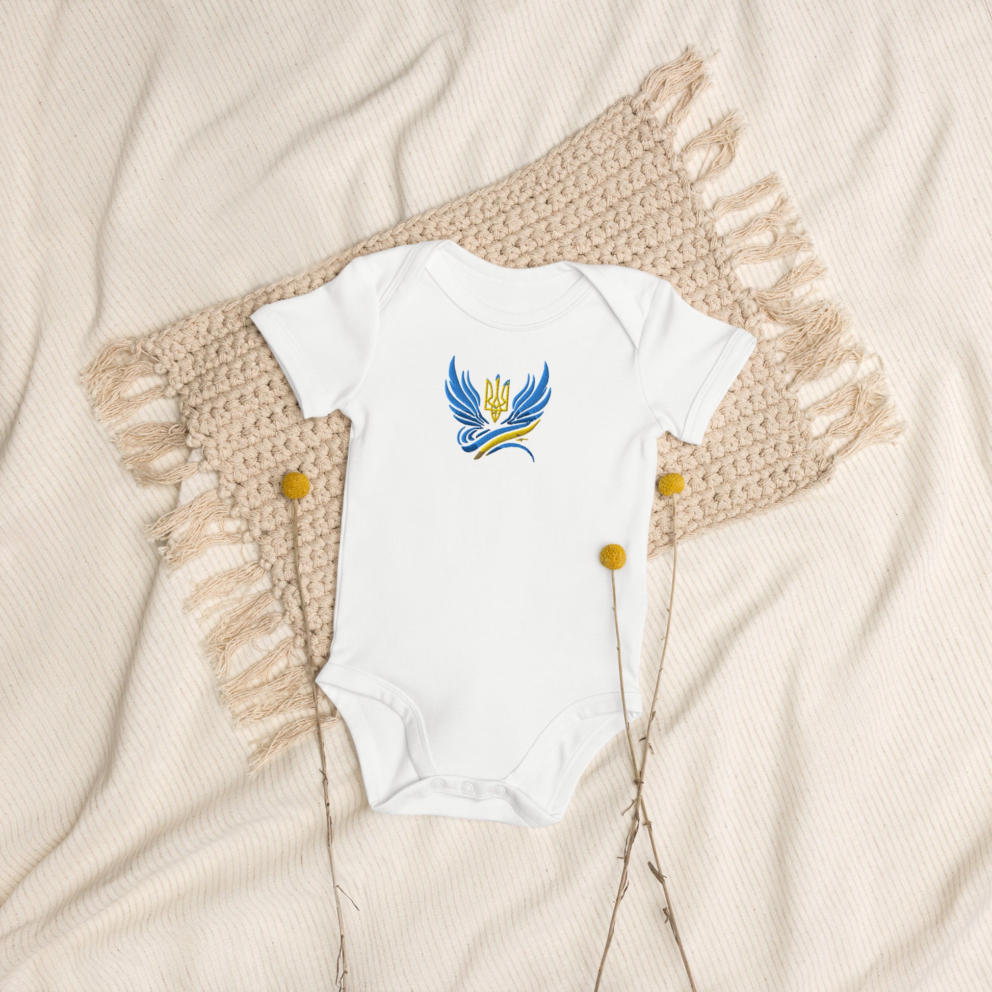 Organic cotton baby bodysuit with Ukrainian Tryzub logo on a textured blanket, highlighting comfort and heritage.