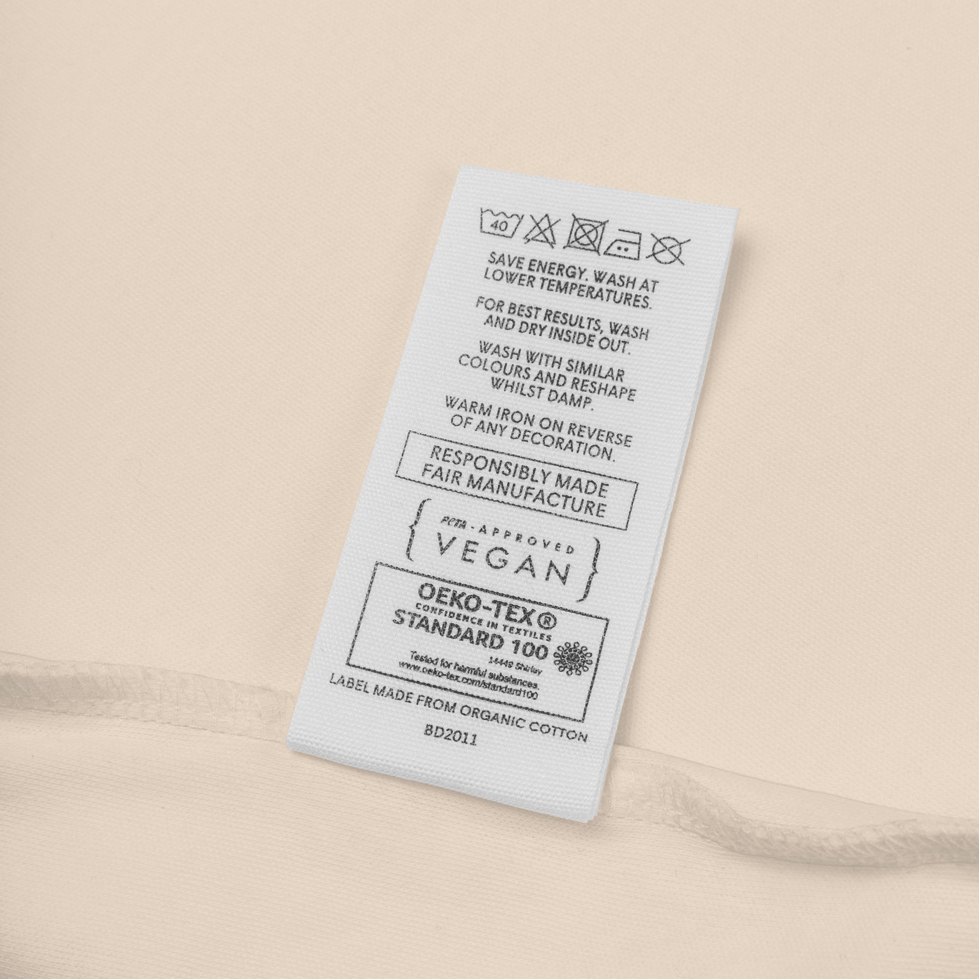 Organic cotton clothing label with vegan and Oeko-Tex certification symbols and care instructions.