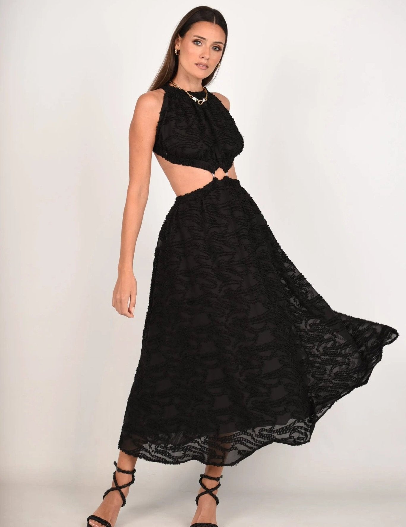 Woman wearing Whispering Jacquard Maxi dress, featuring open back, cinched waist, and airy skirt. Elegant evening wear with black sandals.