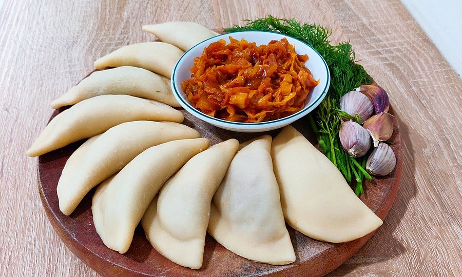 Traditional Ukrainian varenyky with cabbage filling, arranged on a wooden platter with dill and garlic cloves.