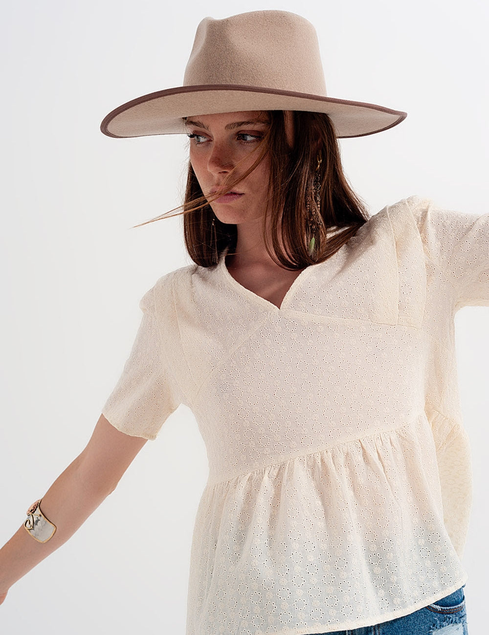 Woman wearing Marcelle Summer Lace Blouse in soft beige cotton, V-neck design, short sleeves, paired with a beige hat.