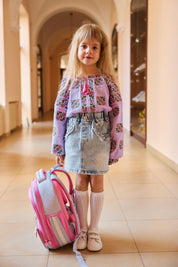 Girl wearing a lavender muslin embroidered vyshyvanka with floral patterns, holding a pink backpack.