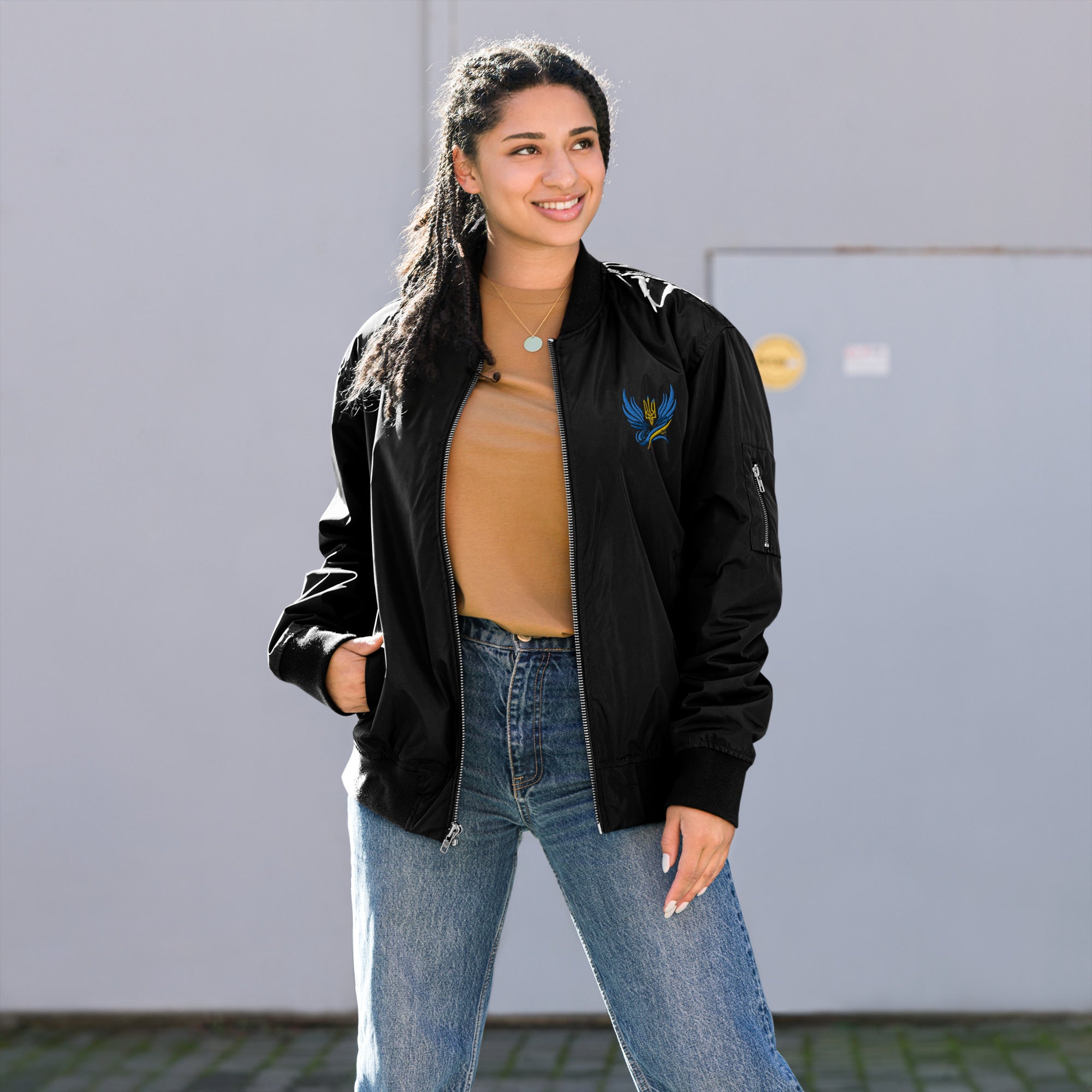 Woman wearing Ukrainian premium recycled bomber jacket with Trizub Collection design, styled with casual outfit outdoors.