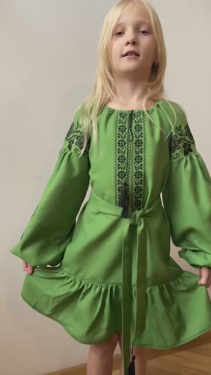 Young girl in green embroidered traditional Ukrainian Vyshyvanka dress with black cross-stitch, boho style for festive occasions.
