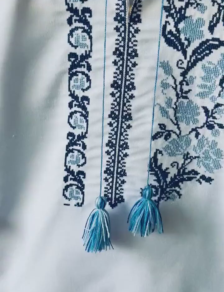 Embroidered Ukrainian boy's vyshyvanka shirt with traditional blue cross-stitch patterns and tassels, perfect for cultural occasions.