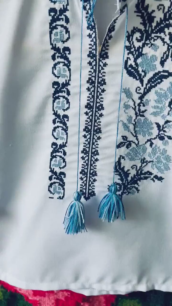 Embroidered Ukrainian boy's vyshyvanka shirt with traditional blue cross-stitch patterns and tassels, perfect for cultural occasions.
