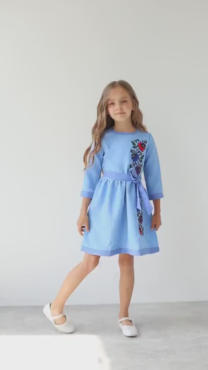 Girl wearing blue Ukrainian embroidered vyshyvanka dress with floral design, celebrating cultural heritage and tradition.