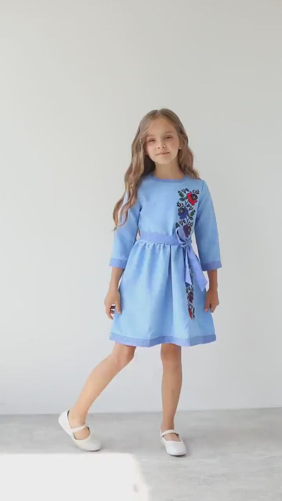Girl wearing blue Ukrainian embroidered vyshyvanka dress with floral design, celebrating cultural heritage and tradition.