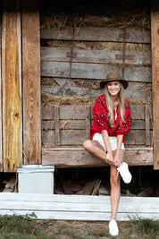 Woman wearing a red linen embroidered blouse, Ukrainian vyshyvanka, sitting in front of a rustic wooden background.