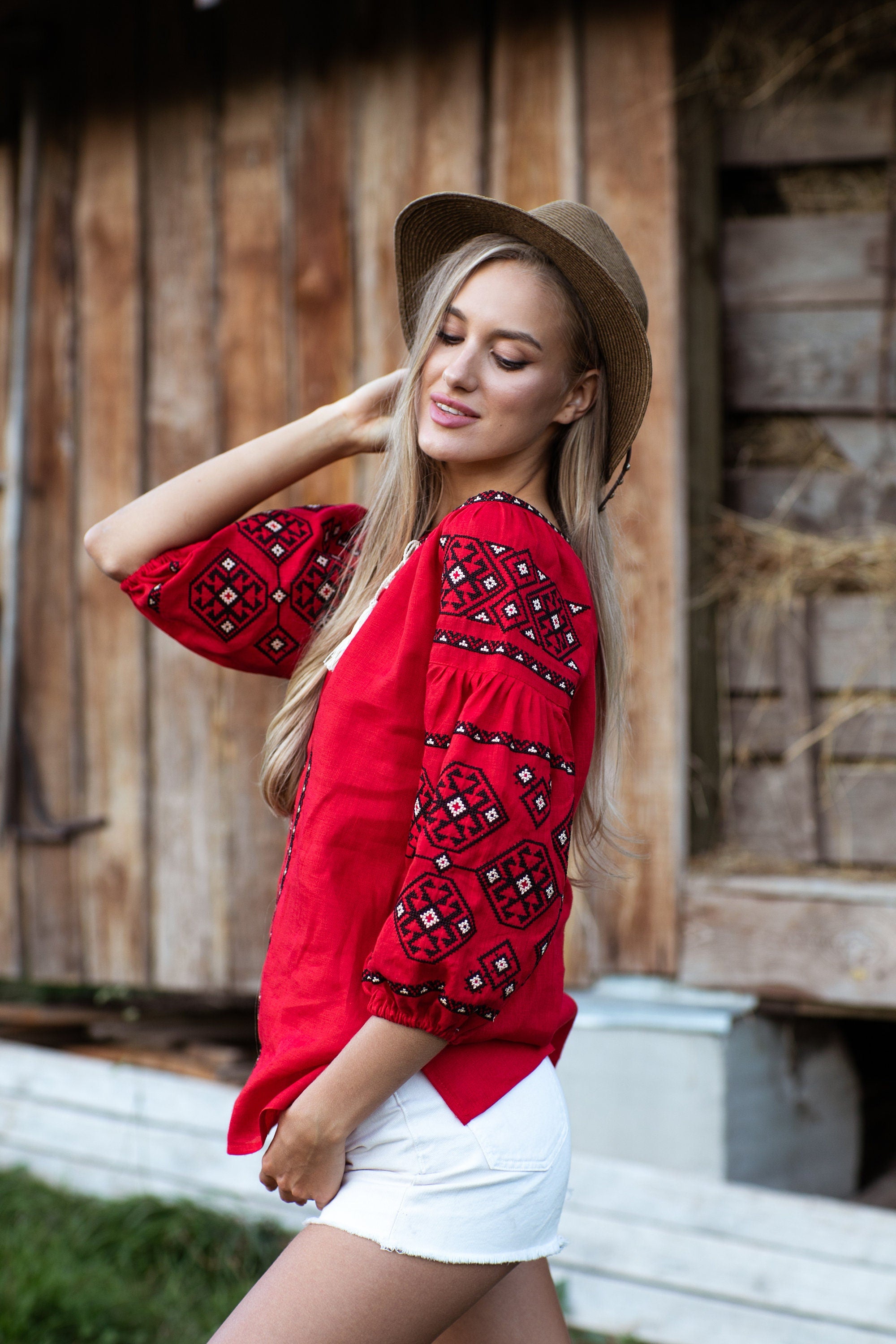Woman wearing red Ukrainian vyshyvanka blouse with traditional embroidery against rustic background