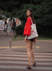 Woman wearing 2025 red linen embroidered blouse in Ukrainian vyshyvanka style, standing with a bag in a casual urban setting.