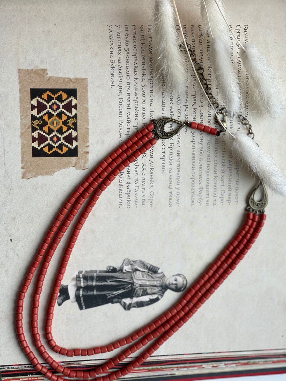Handmade red ceramic beaded necklace, Hutsul style, inspired by Ukrainian ethnic jewelry, set on traditional background.