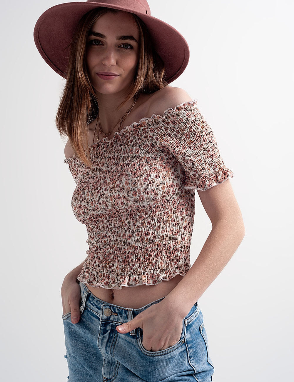 Woman wearing Briselle Bardot Floral Top with ditsy print and Bardot neckline, styled with blue jeans and a pink hat.