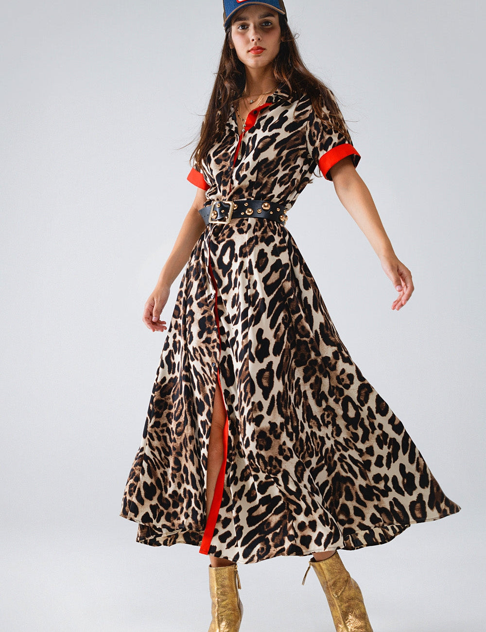 Woman in leopard print dress with red accents and gold boots, wearing a baseball cap.