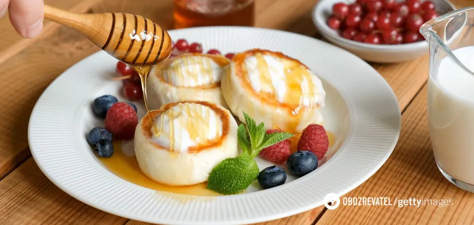 Plate of homemade Ukrainian syrnyky cheese pancakes served with honey, mint, and assorted berries on a wooden table.