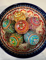 Set of 6 hand-painted wooden eggs in a ceramic bowl, showcasing colorful traditional Ukrainian Pysanky designs.