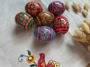 Set of 6 hand-painted Ukrainian wooden Easter eggs with folk art designs, displayed on embroidered fabric.