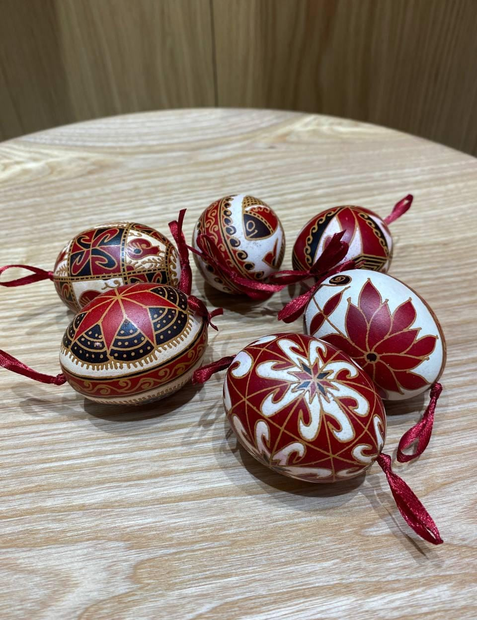 Set of 6 handmade Ukrainian Pysanky eggs with red and white traditional designs on a wooden table, perfect for Easter or Christmas decor.
