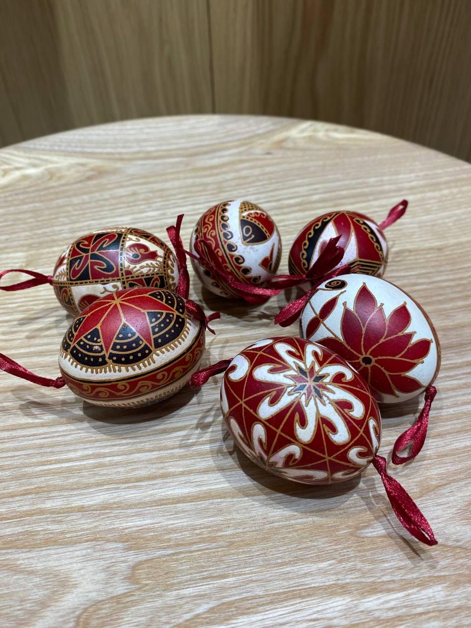 Set of 6 handmade Ukrainian Pysanky eggs with red and white traditional designs on a wooden table, perfect for Easter or Christmas decor.