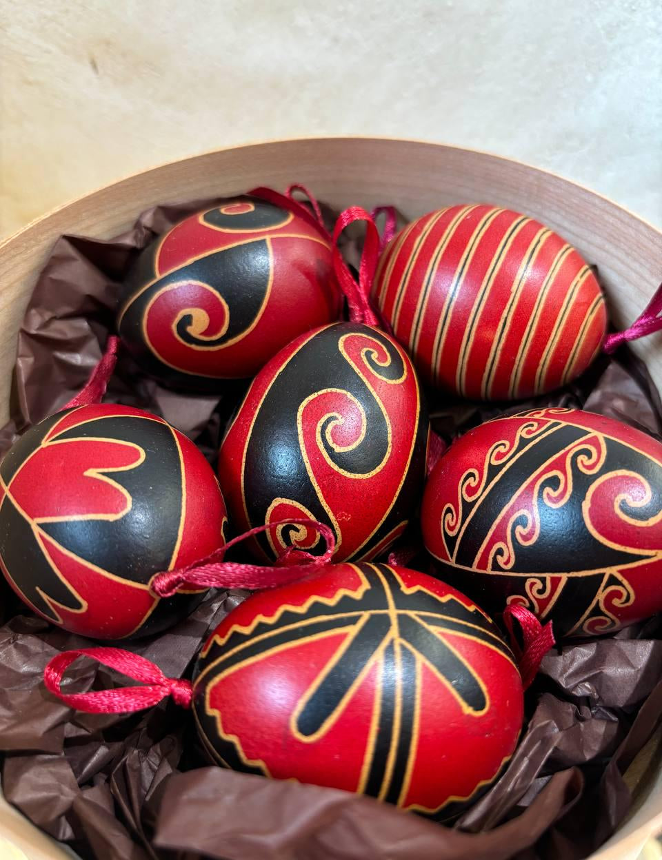 Set of 6 hand-painted Ukrainian Pysanky eggs in a basket, featuring traditional folk art designs and vibrant red and black colors.