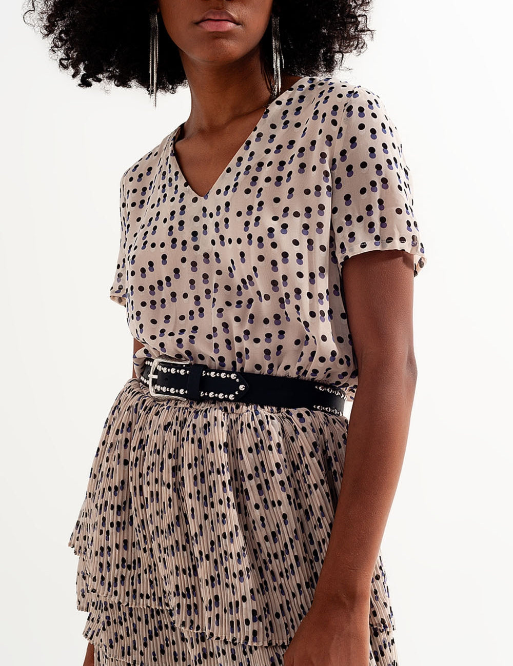 Woman wearing a polka dot pleated dress with a black belt, featuring short sleeves and a V-neckline.
