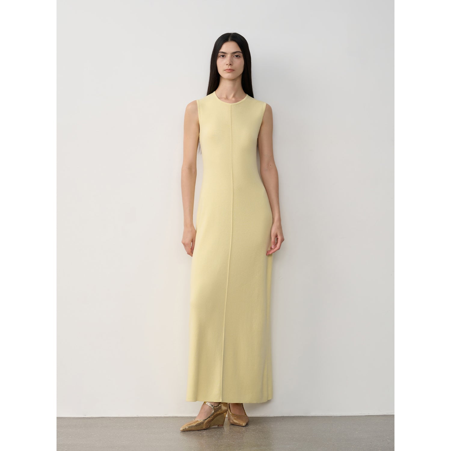 Woman in sleeveless Solenne Merino Wool Maxi Knit Dress with central seam, standing against a white background, showcasing minimalist elegance.